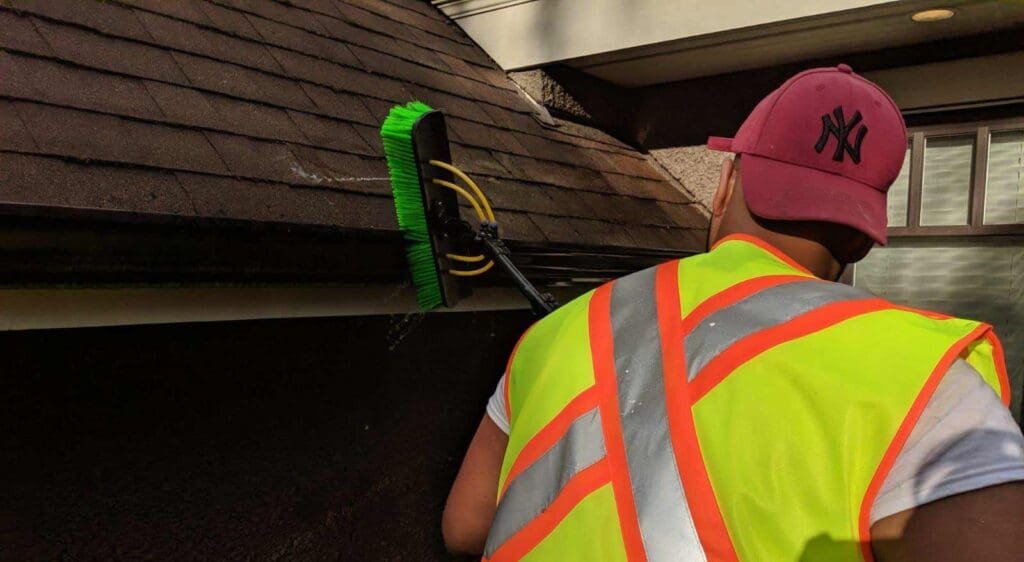 A professional cleaning gutters on a home to prevent damage, showcasing the importance of gutter maintenance.
