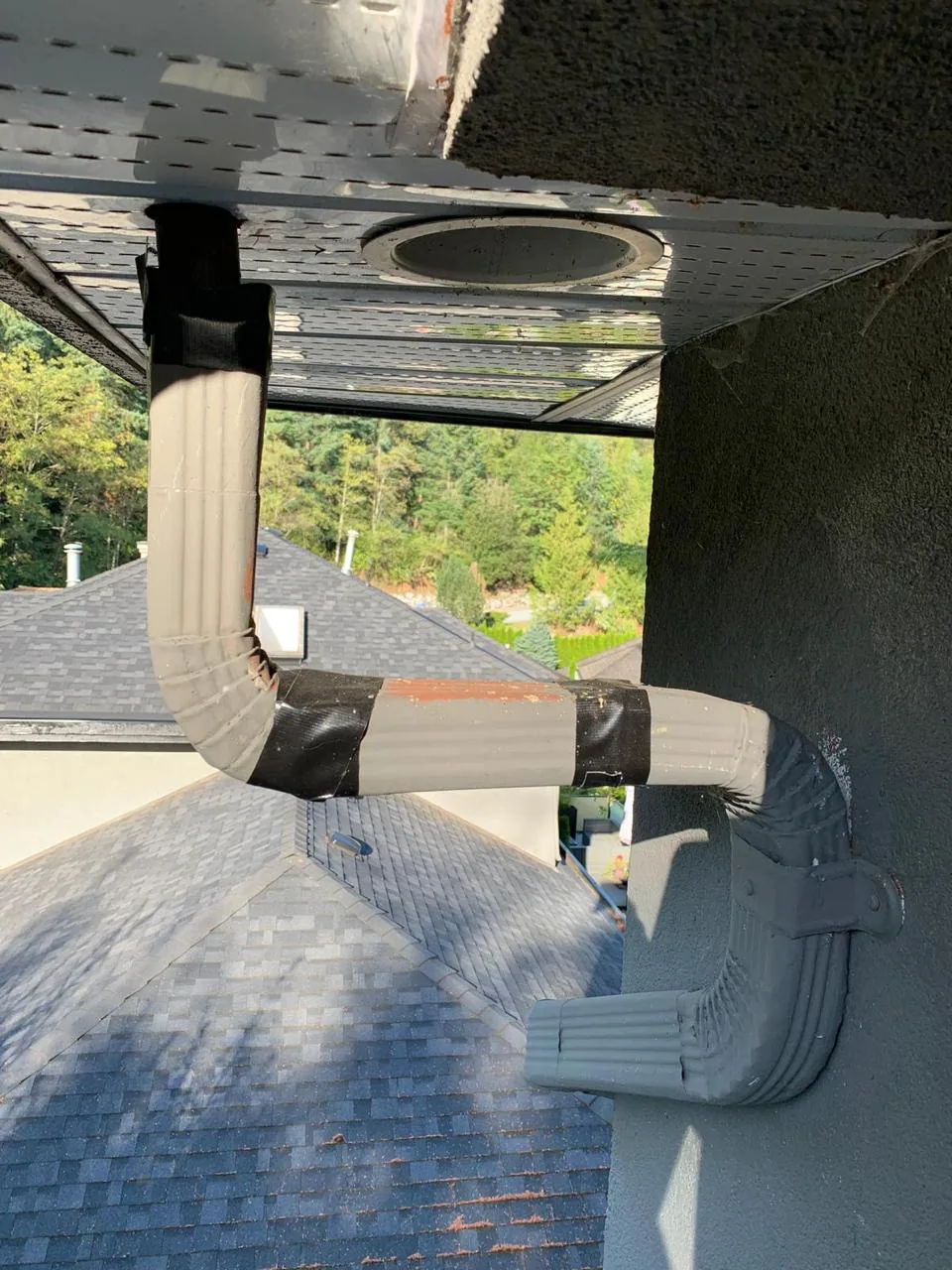 Taped and failing downspout on stucco wall before professional gutter repair in Vancouver BC