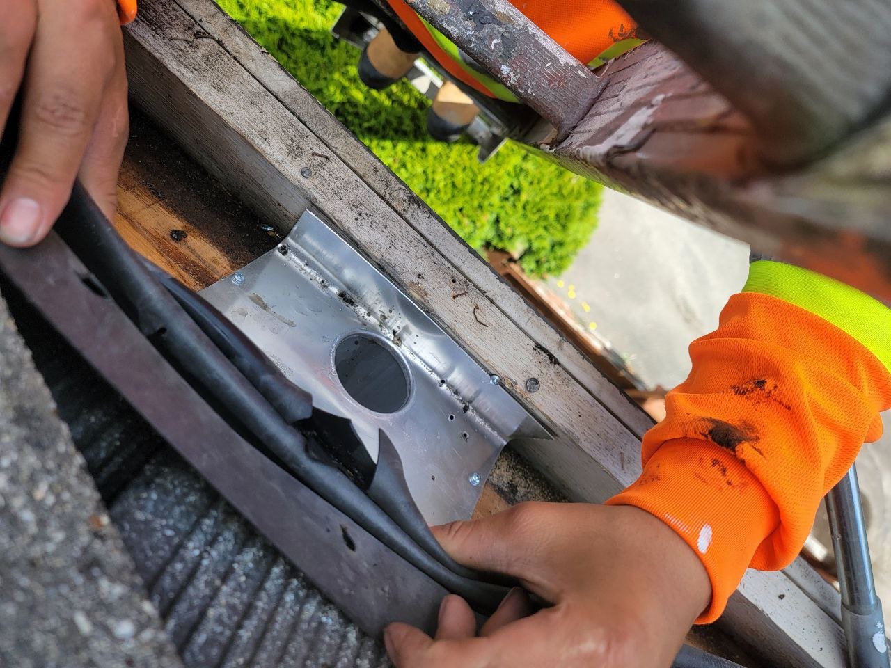 Technician installing custom sheet metal around a built-in gutter downpipe outlet in Vancouver