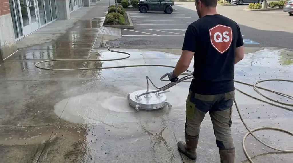 Quick Sidekick technician pressure washing concrete in Vancouver, showing the company uniform