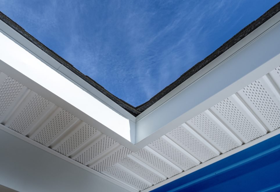 Looking up at newly installed aluminum fascia, perforated soffit and shingles on a residential house with blue siding during a remodeling project.